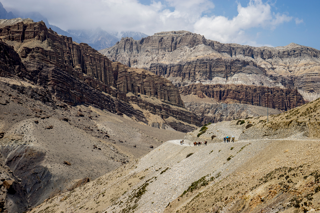 Exploring Western Nepal's Upper Mustang Area, horses and trekkers dwarfed by the surrounding landscape.