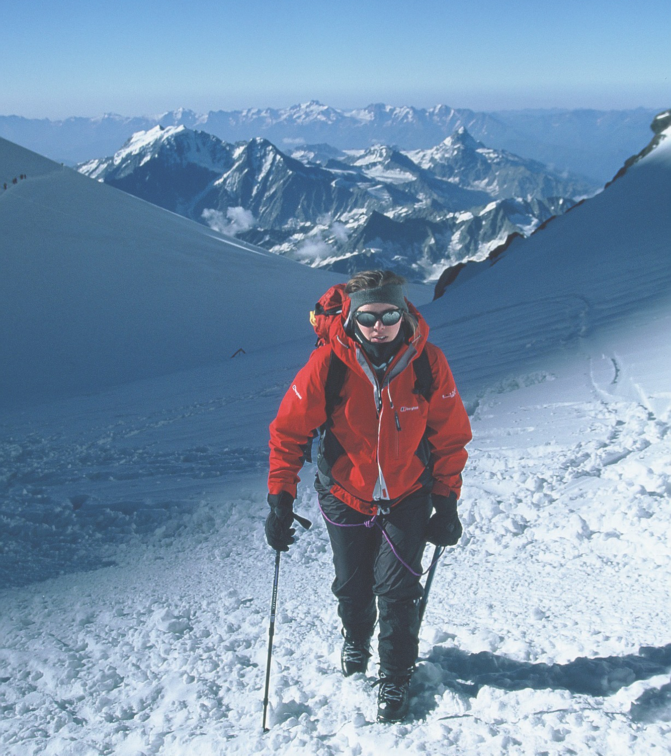 A woman wearing a red jacket climbs up the gully towards the summit of Elbrus