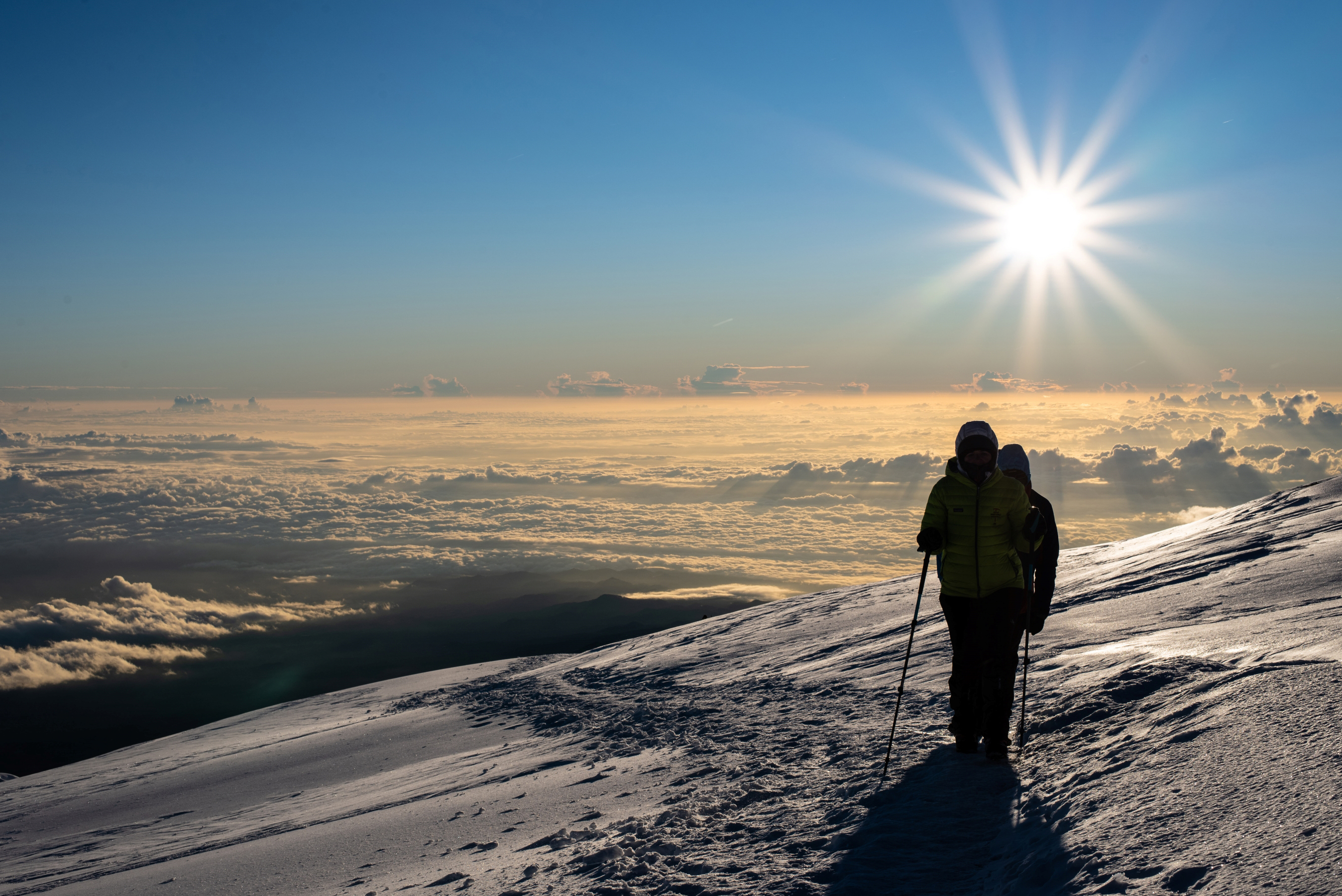 Climbers cross snow slopes as they approach the summit of Kilimanjaro. The morning sun beams behind warming their backs.