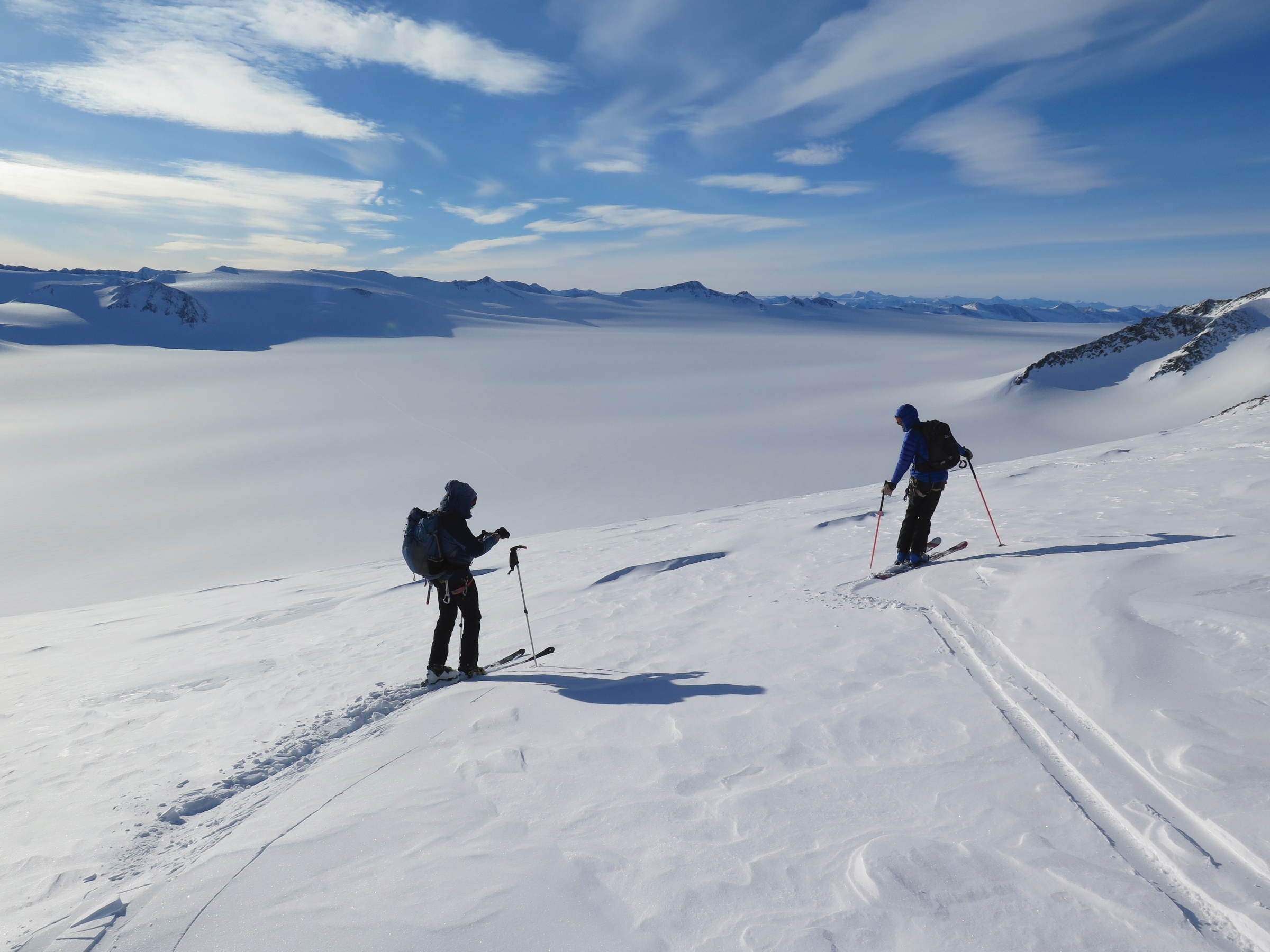 Two skiers contemplate the enormous glacier that fans out between the mountains below them.