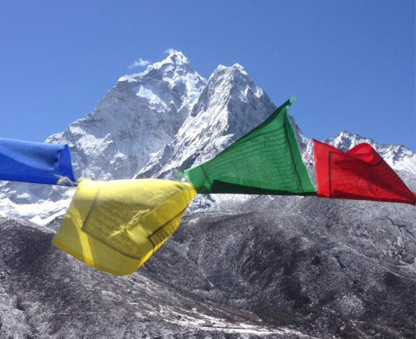 Prayer flags flutter in the breeze with Mount Ama Dablam covered in snow behind.