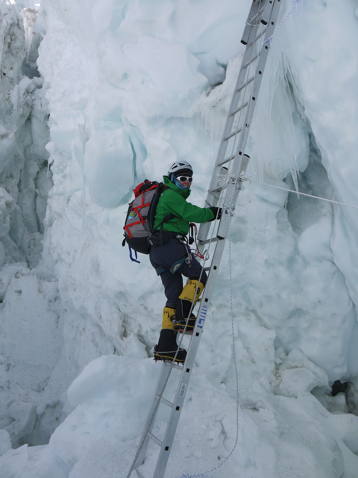 A climber deep in the Khumbu icefall ascends a long ladder made of several ladders tied together.
